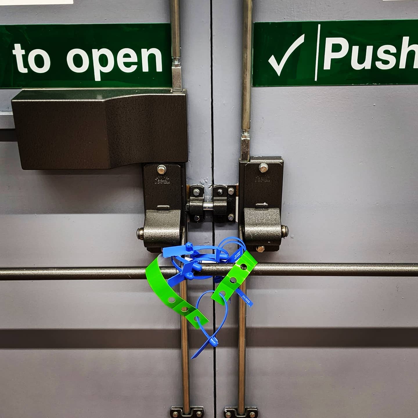 Exit doors at a convention center that have been sealed with various intertwined blue and green tags and zip ties.